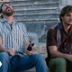 Nic Cage laughing with a mobile phone in his hand, as Pedro Pascal glumly stares while sitting next to him.